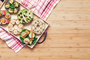 Assorted vegan bagels with plant-based toppings including avocado, tomato, and vegan cream cheese on a wooden board.