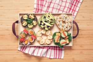 Assorted vegan bagels with plant-based toppings including avocado, tomato, and vegan cream cheese on a wooden board.