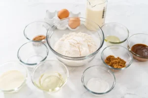 Assorted ingredients for monkey bread recipe including flour, milk, yeast, and cinnamon on a kitchen counter.