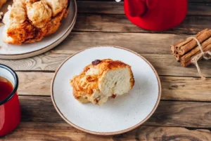 Freshly baked monkey bread on a serving plate, showing its golden caramelized crust and pull-apart texture, surrounded by cinnamon sticks and sugar for decoration.