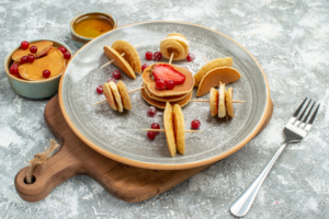 Assorted mini pancakes with berries, whipped cream, and nuts on a brunch table.