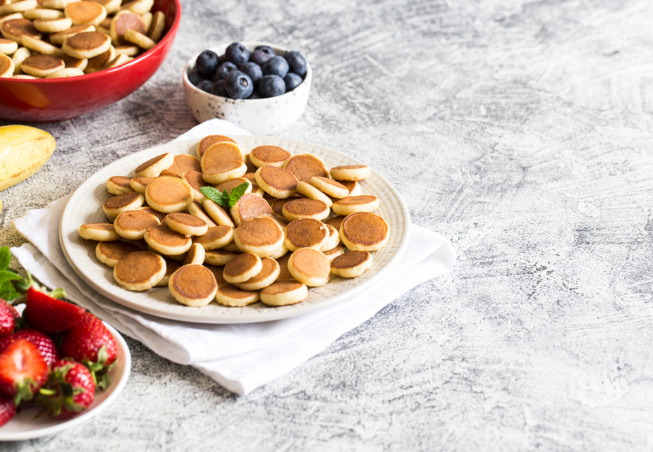 Creative presentation of mini pancakes shaped like a flower with berry center.