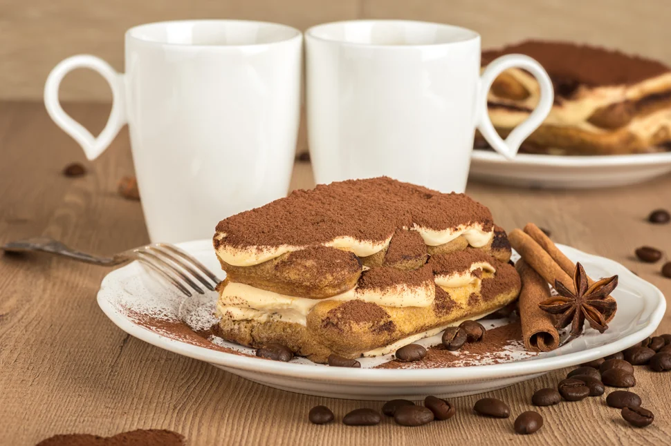 A delectable slice of classic tiramisu sits on a white plate, its layers of espresso-soaked ladyfingers, creamy mascarpone, and a dusting of cocoa powder highlighted in the soft light, inviting a closer look at this beloved Italian dessert and its caffeine content.