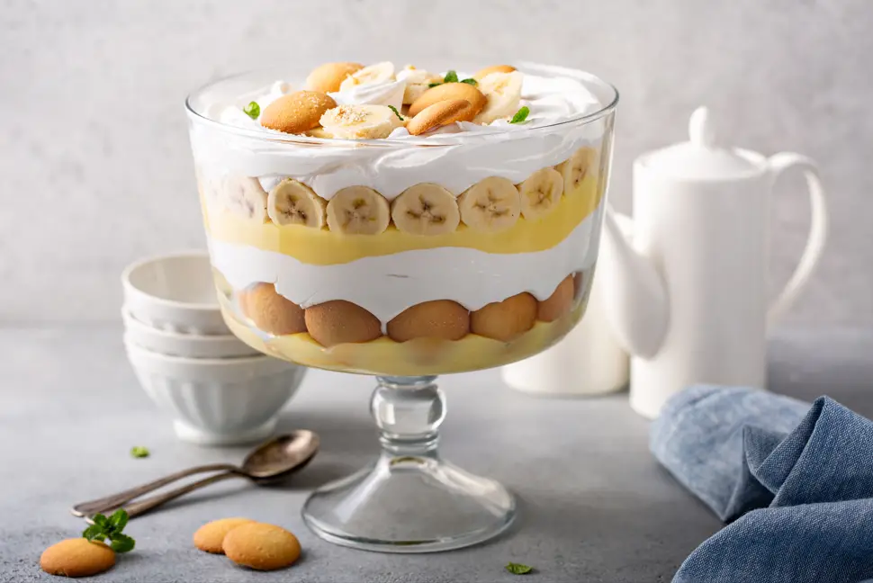 A delectable bowl of banana pudding, featuring layers of creamy, rich vanilla custard, ripe banana slices, and crunchy Nilla Wafers, topped with a fluffy whipped cream garnish and a sprinkle of crushed cookies for an extra touch of sweetness and texture.