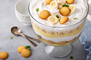 A delectable bowl of banana pudding, featuring layers of creamy, rich vanilla custard, ripe banana slices, and crunchy Nilla Wafers, topped with a fluffy whipped cream garnish and a sprinkle of crushed cookies for an extra touch of sweetness and texture.