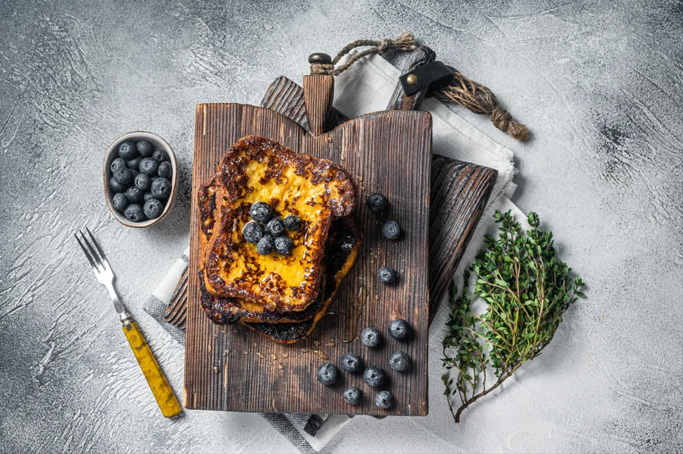 Golden-brown brioche French toast topped with fresh berries and a drizzle of maple syrup on a white plate