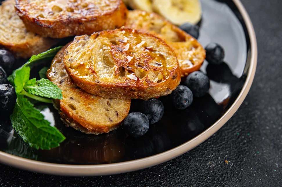 Golden brown French toast on a plate with maple syrup drizzle and fresh berries