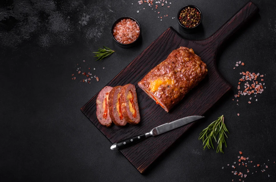 Juicy smoked meatloaf on a wooden cutting board, garnished with fresh herbs, ready to be served