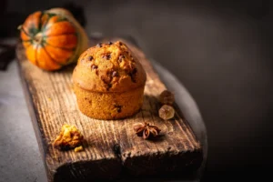 Close-up of a homemade pumpkin muffin on a rustic wooden table, highlighting its moist texture and autumnal spices, with a focus on low-carb baking alternatives.